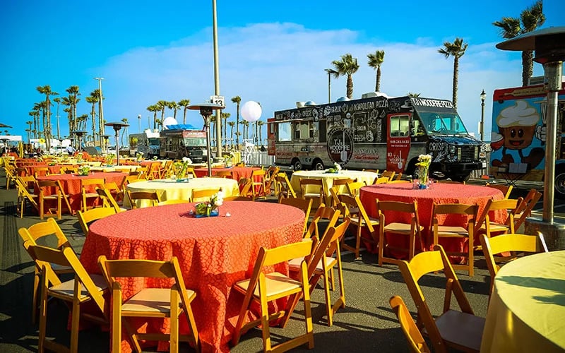 Outdoor food truck event with orange tables and tellow chairs during the day